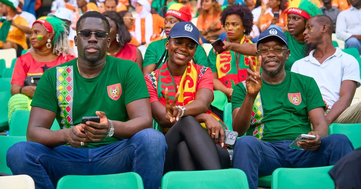Des fans dans un stade de football montrant de l'enthousiasme et faisant des signes de paix, profitant du match en direct.