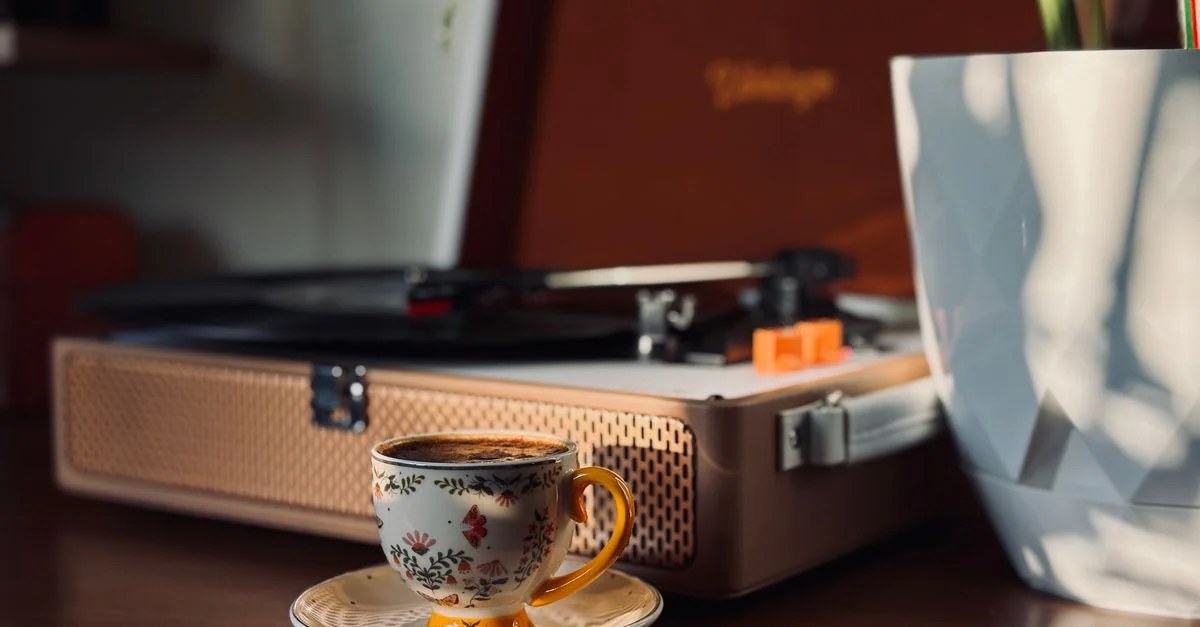 Un décor chaleureux et vintage avec une tasse à café à motifs floraux, un tourne-disque et une plante en pot baignés d'une douce lumière naturelle.