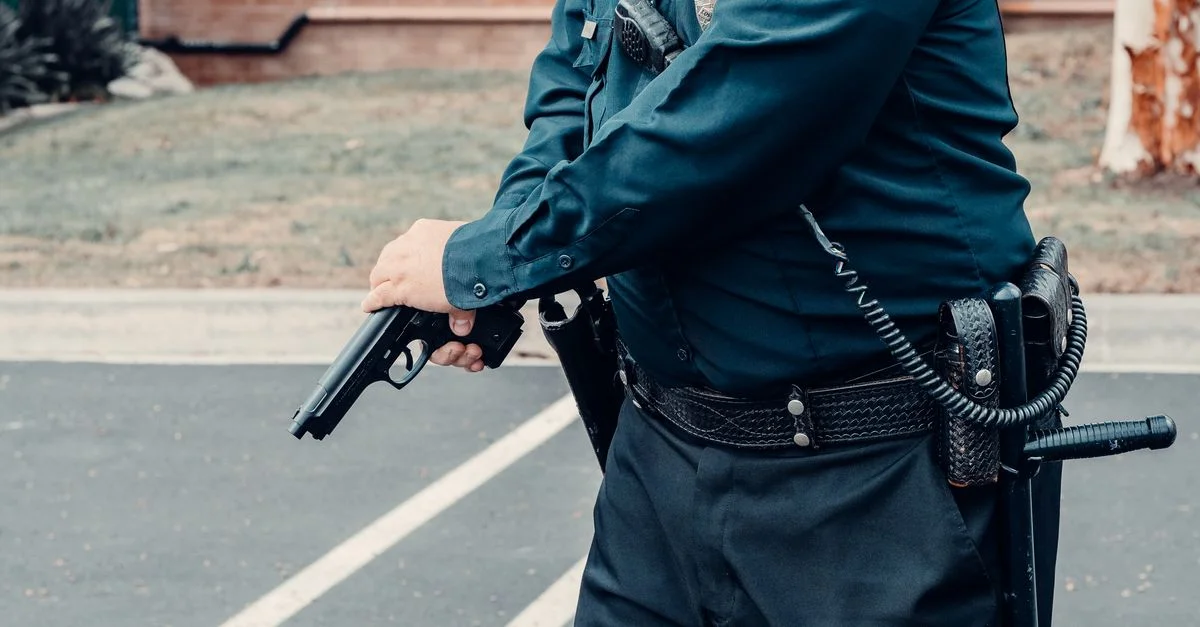 Un agent de police ajustant une arme à feu en extérieur dans une situation tactique, veillant à la sécurité.