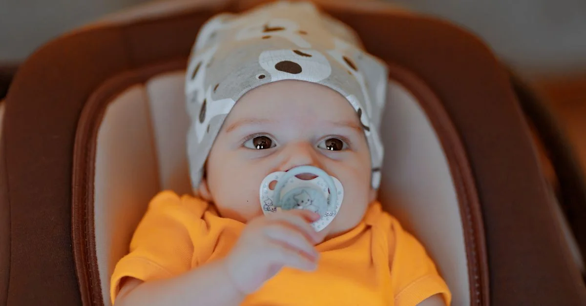 Bébé adorable avec un bonnet et une tétine dans un t-shirt orange, à l'intérieur.