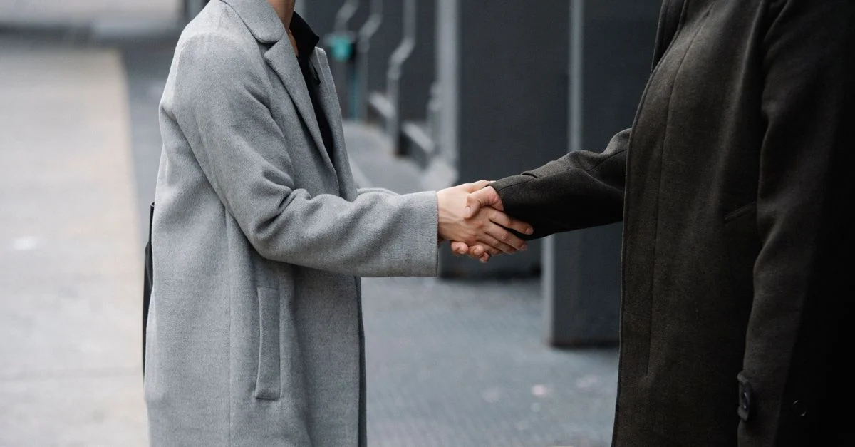 Deux professionnels en manteaux serrant la main dans une rue urbaine, symbolisant la coopération.