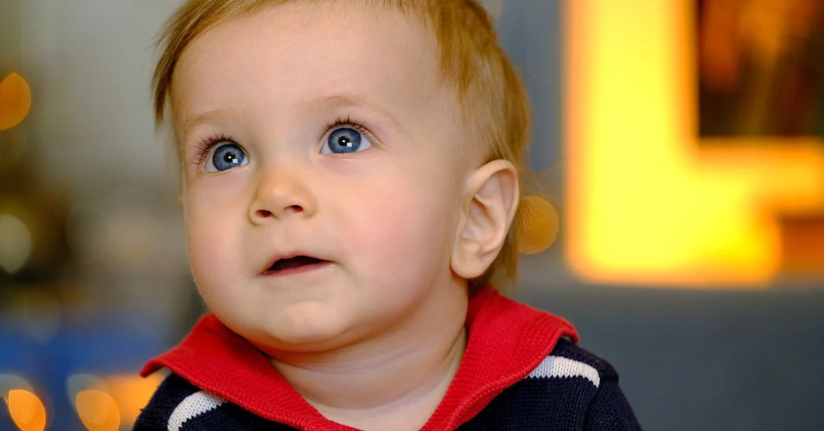 Photo candide d'un bébé aux yeux bleus regardant vers le haut dans un cadre intérieur confortable.