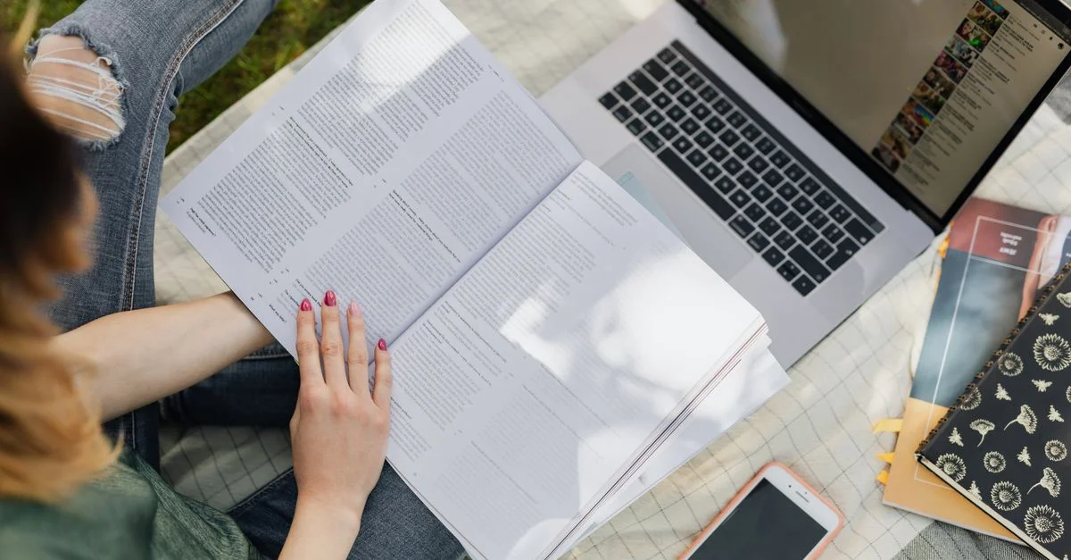 Jeune femme étudiant en plein air avec un ordinateur portable, un carnet et un smartphone dans un parc.