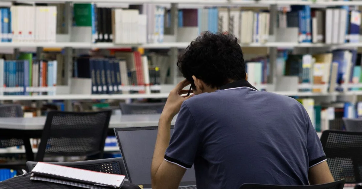 Un jeune adulte concentré sur ses études dans une bibliothèque de Monterrey, utilisant un ordinateur portable et ses notes.