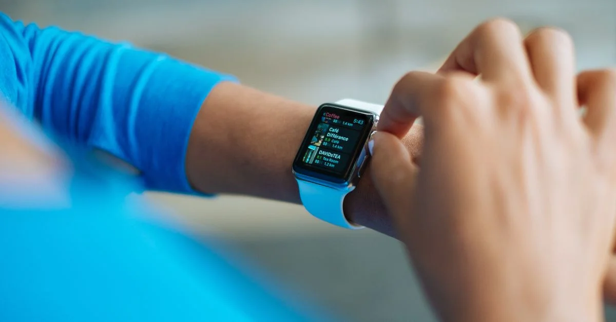 Personne interagissant avec une montre intelligente, affichant une application de fitness à l'écran.