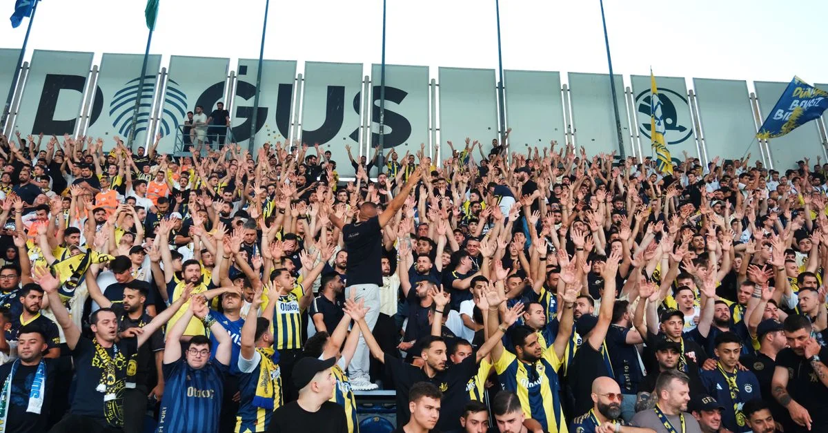 Des supporters enthousiastes, soutenant leur équipe dans un stade de football plein à craquer, lèvent les mains à l'unisson.
