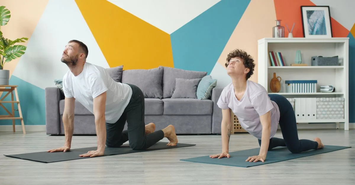 Un couple faisant du yoga sur des tapis dans un salon moderne et coloré.
